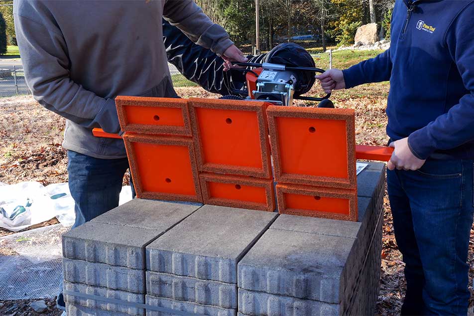 Two people using a brick cutting machine on a stack of bricks outdoors.