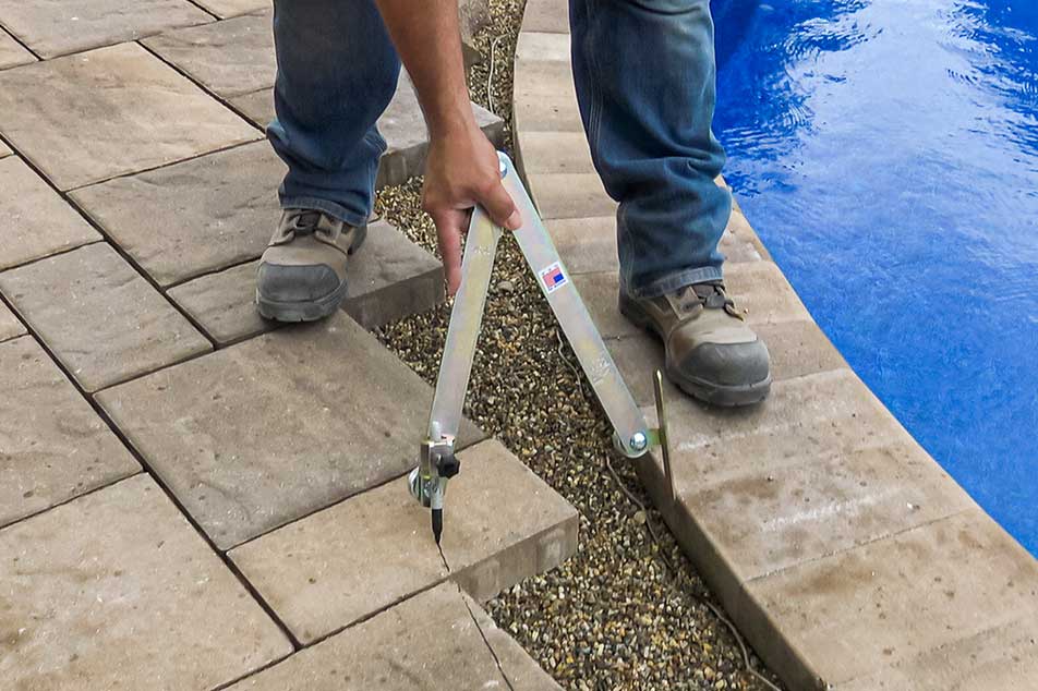 Person using a tool on a stone patio next to a pool